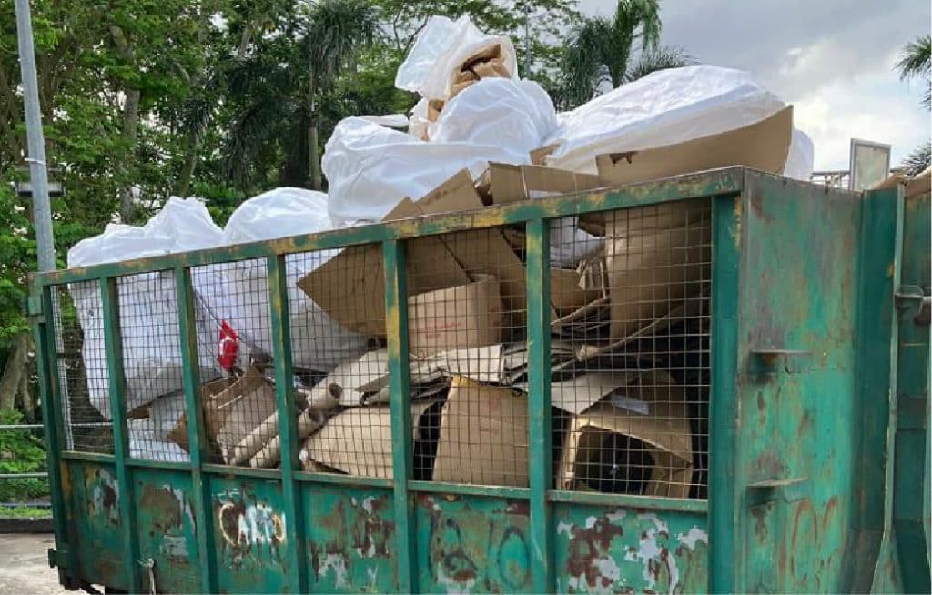 A large green industrial bin filled with cardboard and plastic for general waste disposal services.